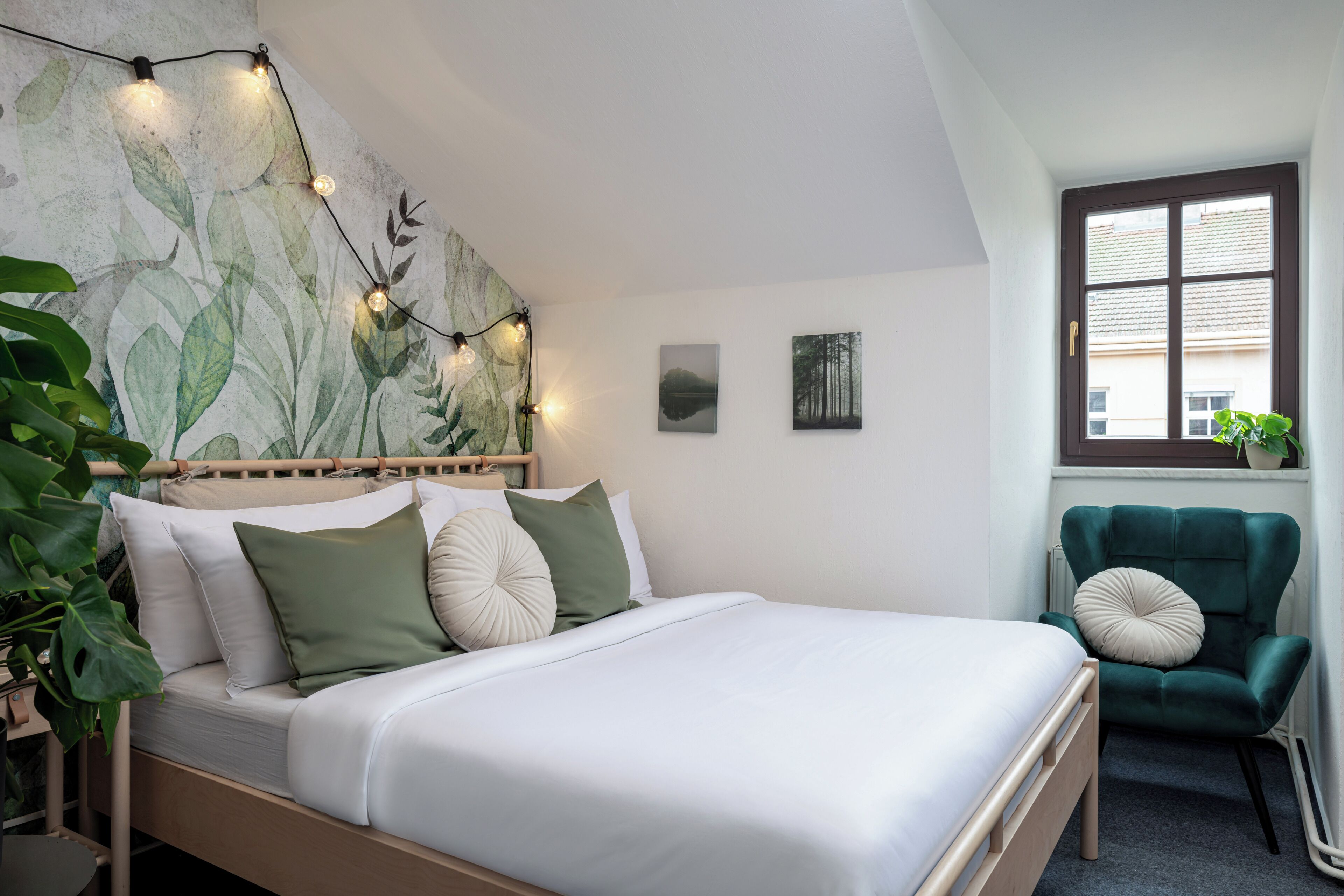 Ein Schlafzimmer mit einem Bett, einem grünen Sessel, einem Fenster und einer Wand mit einem Blattmuster.