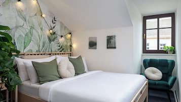 A bedroom with a bed, a green armchair, a window, and a wall with a leaf pattern.