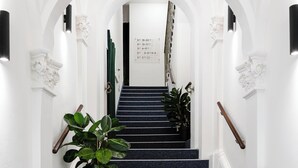 Una escalera con paredes blancas y alfombra azul, que lleva a una puerta con un cartel.