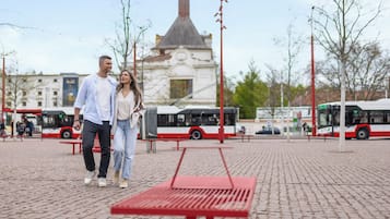 A couple walking on a paved area with benches and buses in the background.