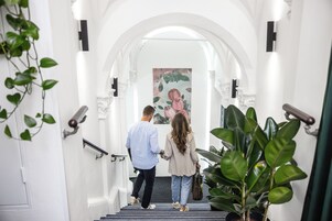 Una escalera con paredes blancas, un cuadro floral en la parte superior y una barandilla a la izquierda.