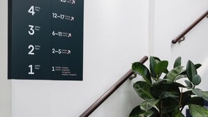 Una escalera con barandilla negra, una planta en maceta y un cartel en la pared que indica los números de habitación y sus tipos.