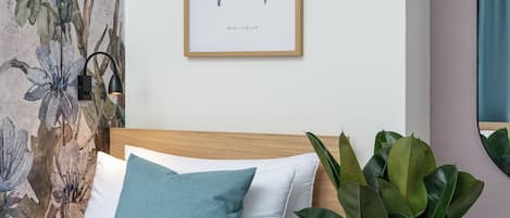 A bed with a wooden headboard, a blue pillow, and a white pillow. There is a framed butterfly artwork on the wall.