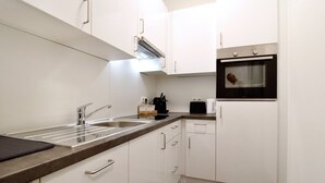 A modern kitchen with white cabinets, a stainless steel sink, and an oven. - Stylish Home in Vienna’s Central 9th District (Vienna)