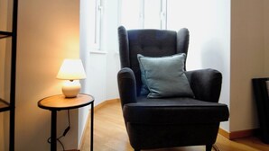 A room with a dark armchair, a small round table with a lamp, and a window with blinds. - Stylish Home in Vienna’s Central 9th District (Vienna)