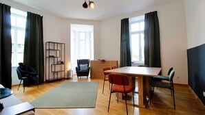 A modern living room with a wooden floor, a dining table with chairs, a sofa, a bookshelf, and a large window with curtains. - Stylish Home in Vienna’s Central 9th District (Vienna)