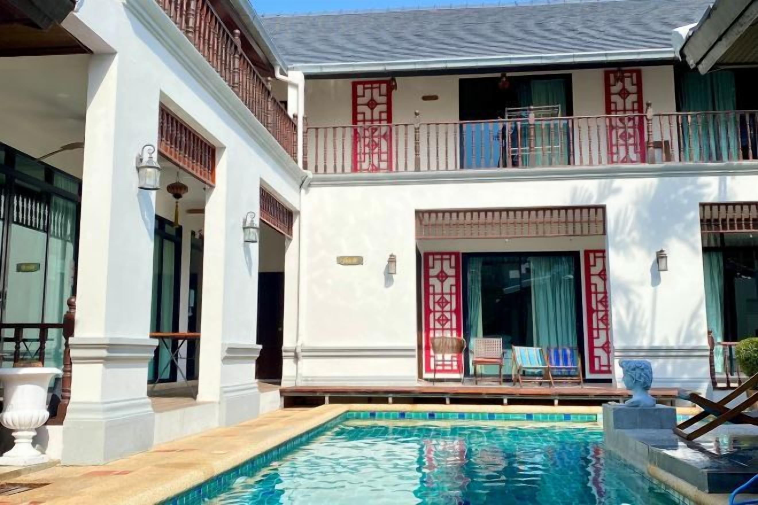 Un bâtiment à deux étages doté d’une piscine, de balcons et d’un espace extérieur aménagé avec des sièges, protégé par un auvent.