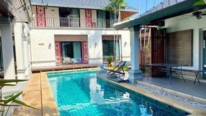 A swimming pool with a tiled deck, a covered seating area, and a building with a balcony. - Taurus Villa10 Bedrooms with Private Pool. (Pattaya)