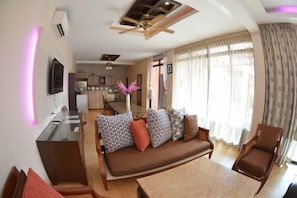 A living room with a sofa, a dining table, and a ceiling fan. - Taurus Villa10 Bedrooms with Private Pool. (Pattaya)