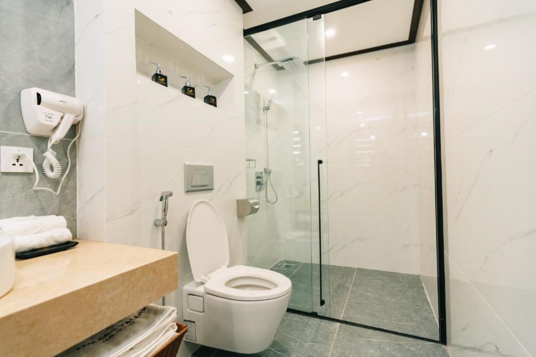 A modern bathroom with a glass-enclosed shower, a white toilet, and a vanity with a hairdryer.