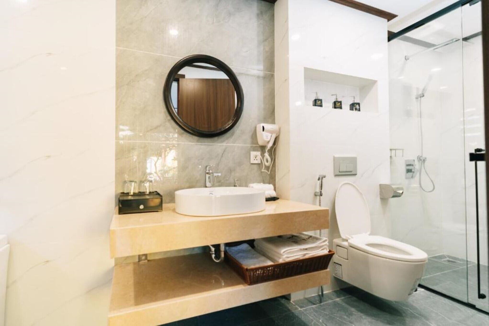 Une salle de bain moderne avec un grand miroir rond, un lavabo, des toilettes et une douche à parois de verre.