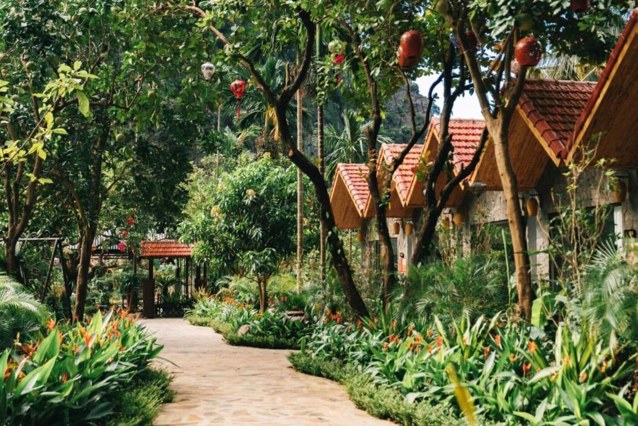 A pathway leading through a lush garden with traditional-style buildings with red-tiled roofs.