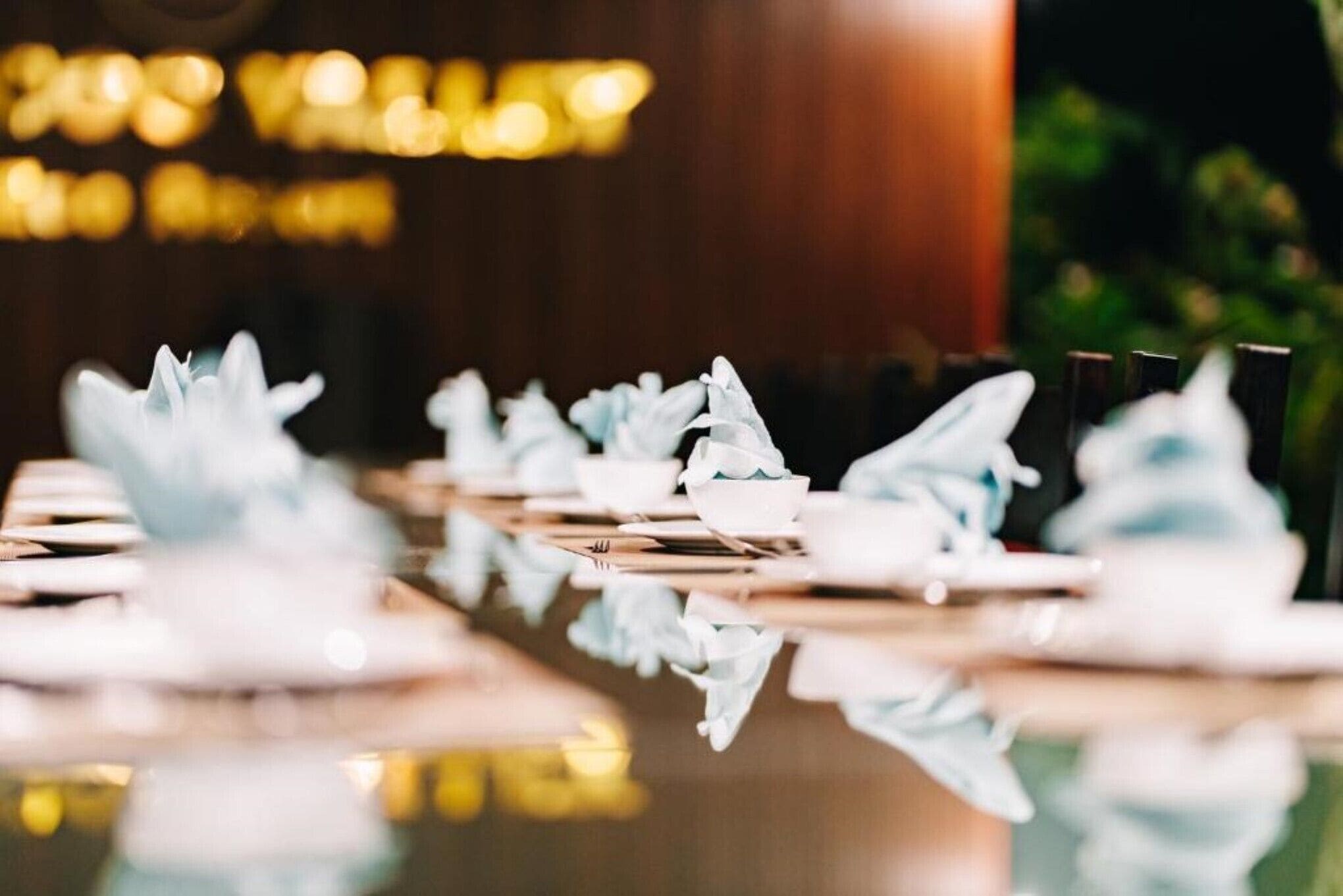 Una mesa de comedor con servilletas y platos blancos, cuyo reflejo se aprecia en la superficie pulida.