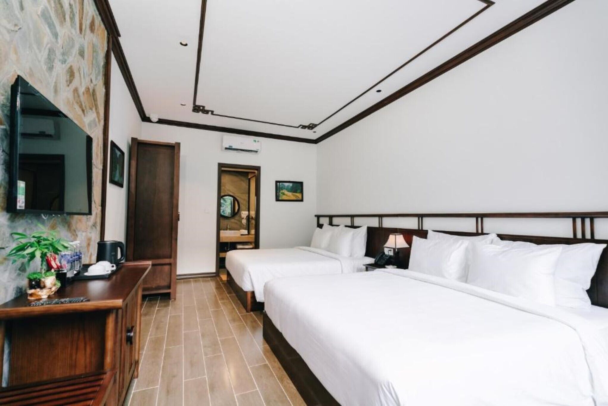 Une chambre d’hôtel avec deux lits, un bureau en bois, un téléviseur à écran plat et un mur en pierre.
