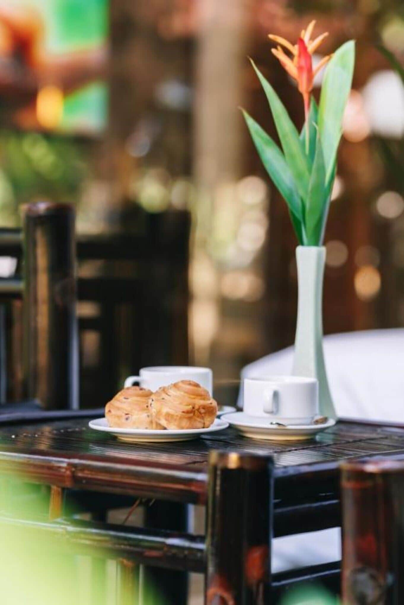 A table with a white vase containing a plant, a plate with pastries, and a cup.