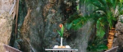 A table with two chairs in front of a rocky wall with a waterfall.