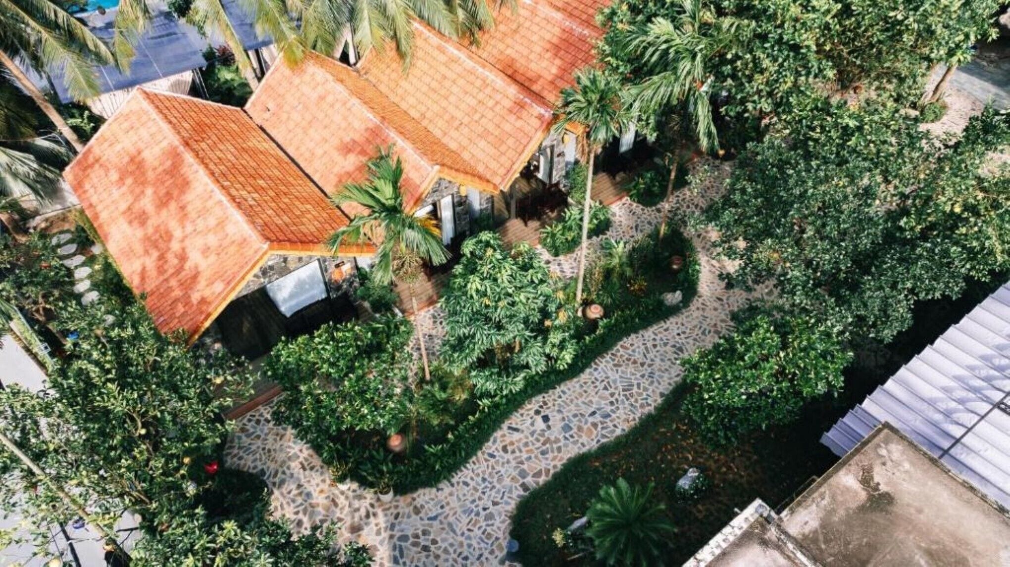 An aerial view of a courtyard with a tiled roof, surrounded by lush greenery and a stone pathway.
