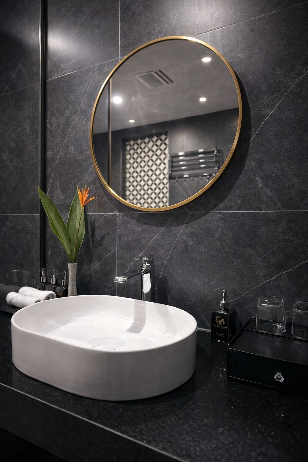 Un baño moderno con un espejo redondo, un lavabo blanco y una encimera negra.