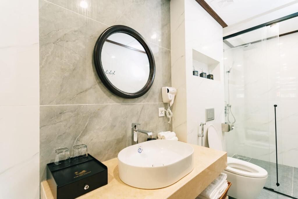 A modern bathroom with a marble sink, a round mirror, and a glass-enclosed shower.