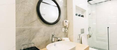 A modern bathroom with a marble sink, a round mirror, and a glass-enclosed shower.