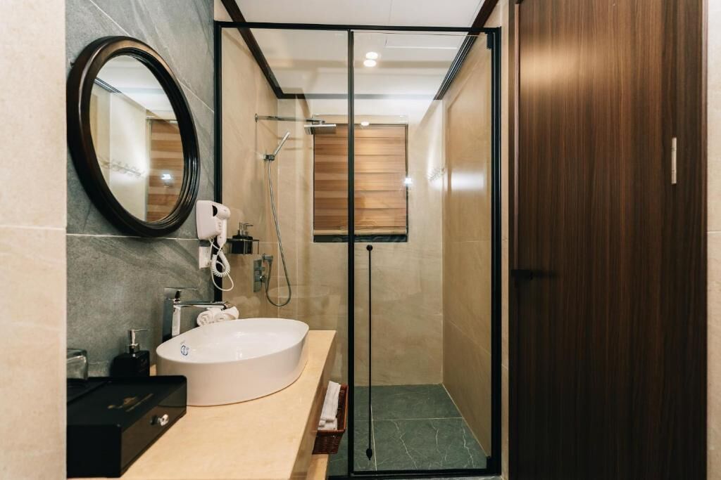 Une salle de bain moderne avec un grand lavabo ovale, une douchette à main et une douche à l’italienne avec des parois en verre.