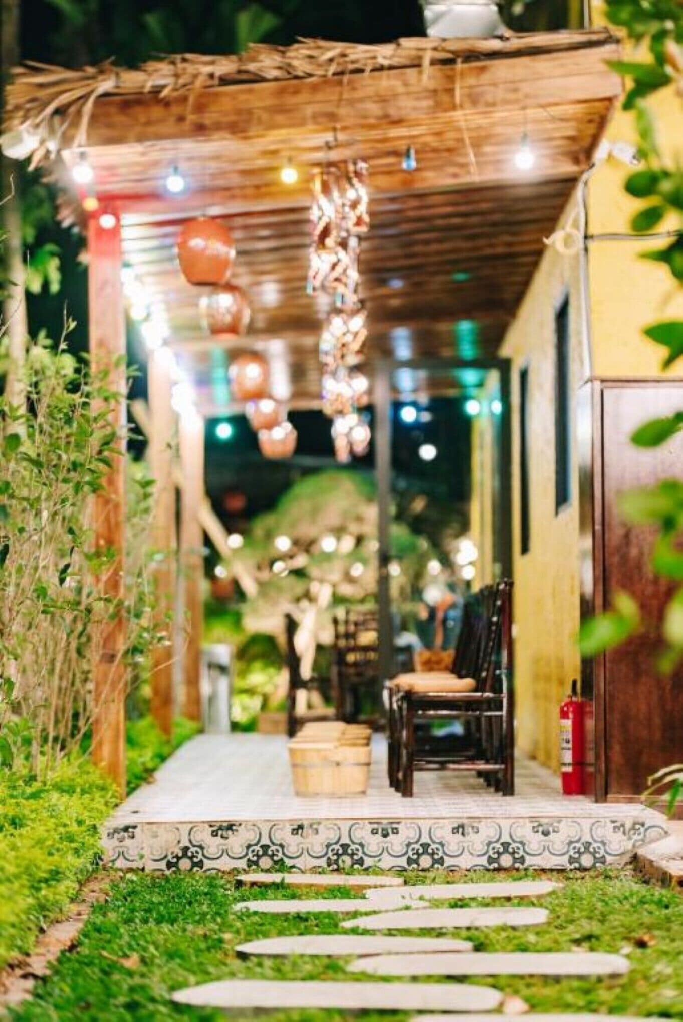 A cozy outdoor seating area with a wooden pergola, string lights, and a fire extinguisher.