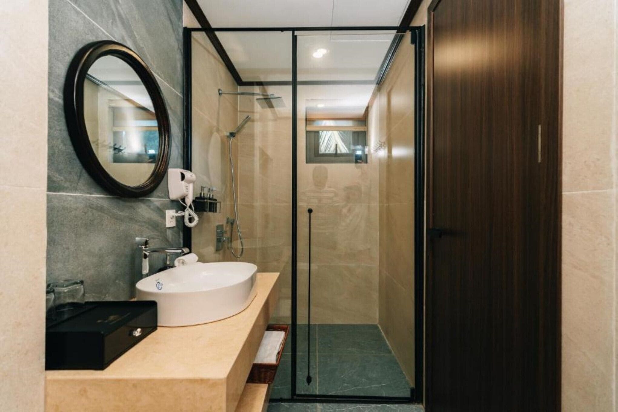 A modern bathroom with a large oval mirror, a white sink, and a glass-enclosed shower.
