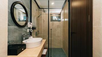A modern bathroom with a large oval mirror, a white sink, and a glass-enclosed shower.