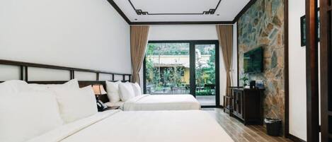 Habitación de hotel con una cama grande, televisión, pared decorativa de piedra y vista a zonas verdes.
