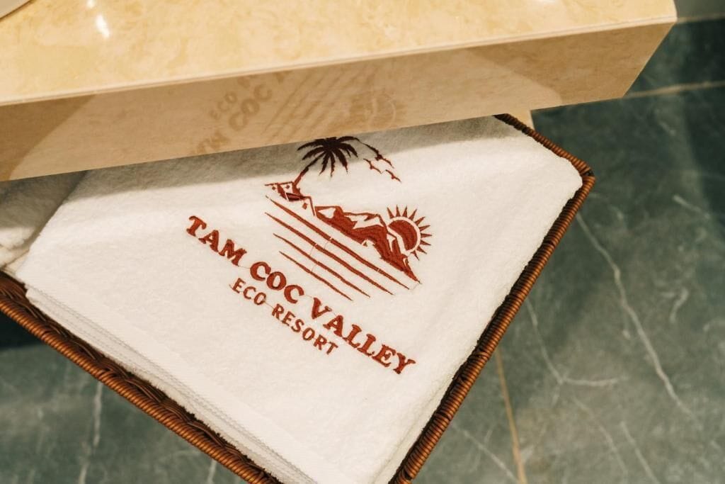 A white towel with 'TAM COC VALLEY ECO RESORT' printed on it, placed on a wicker basket.