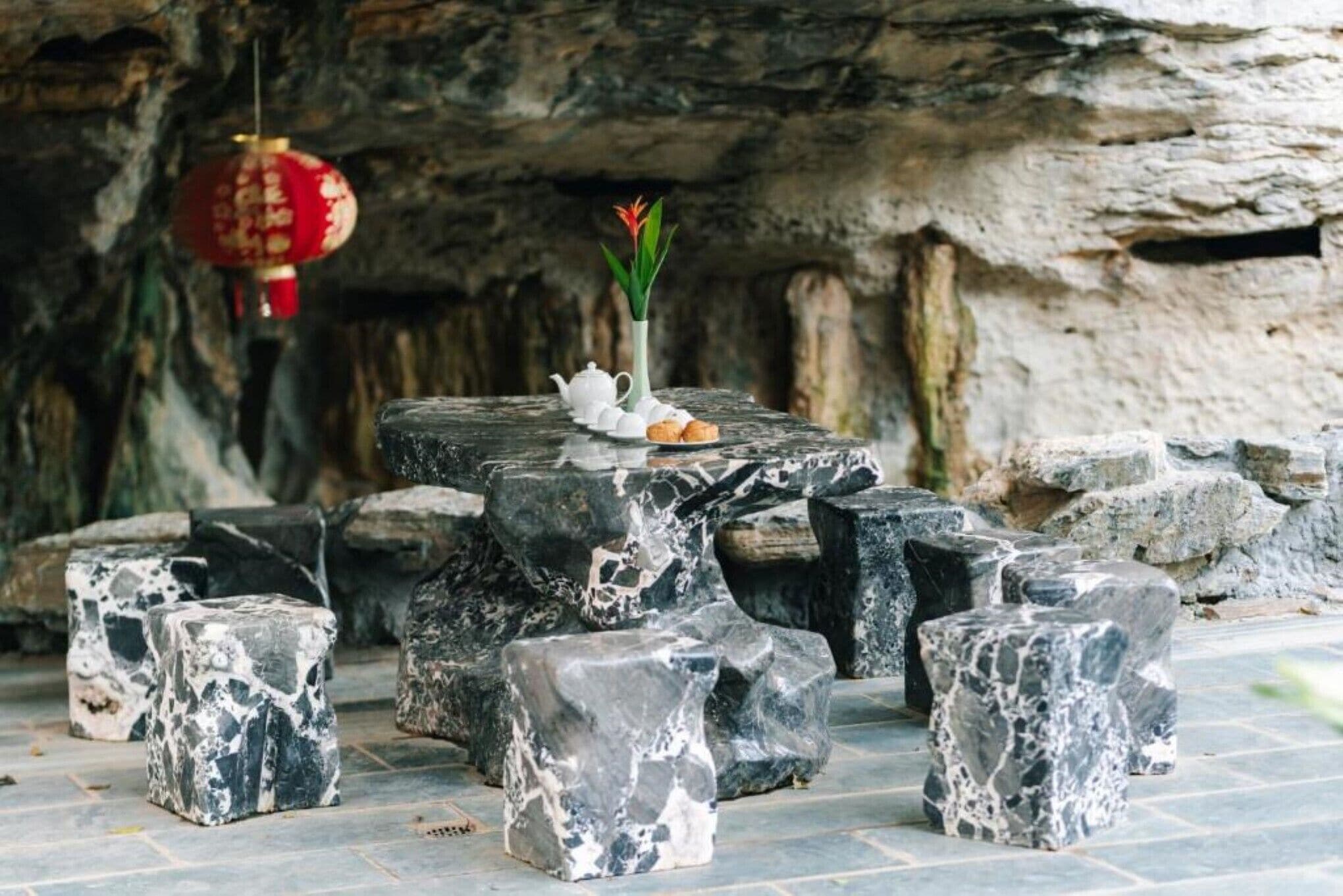 A stone table with a vase of flowers and a teapot, surrounded by irregularly shaped stone stools in a cave-like setting.