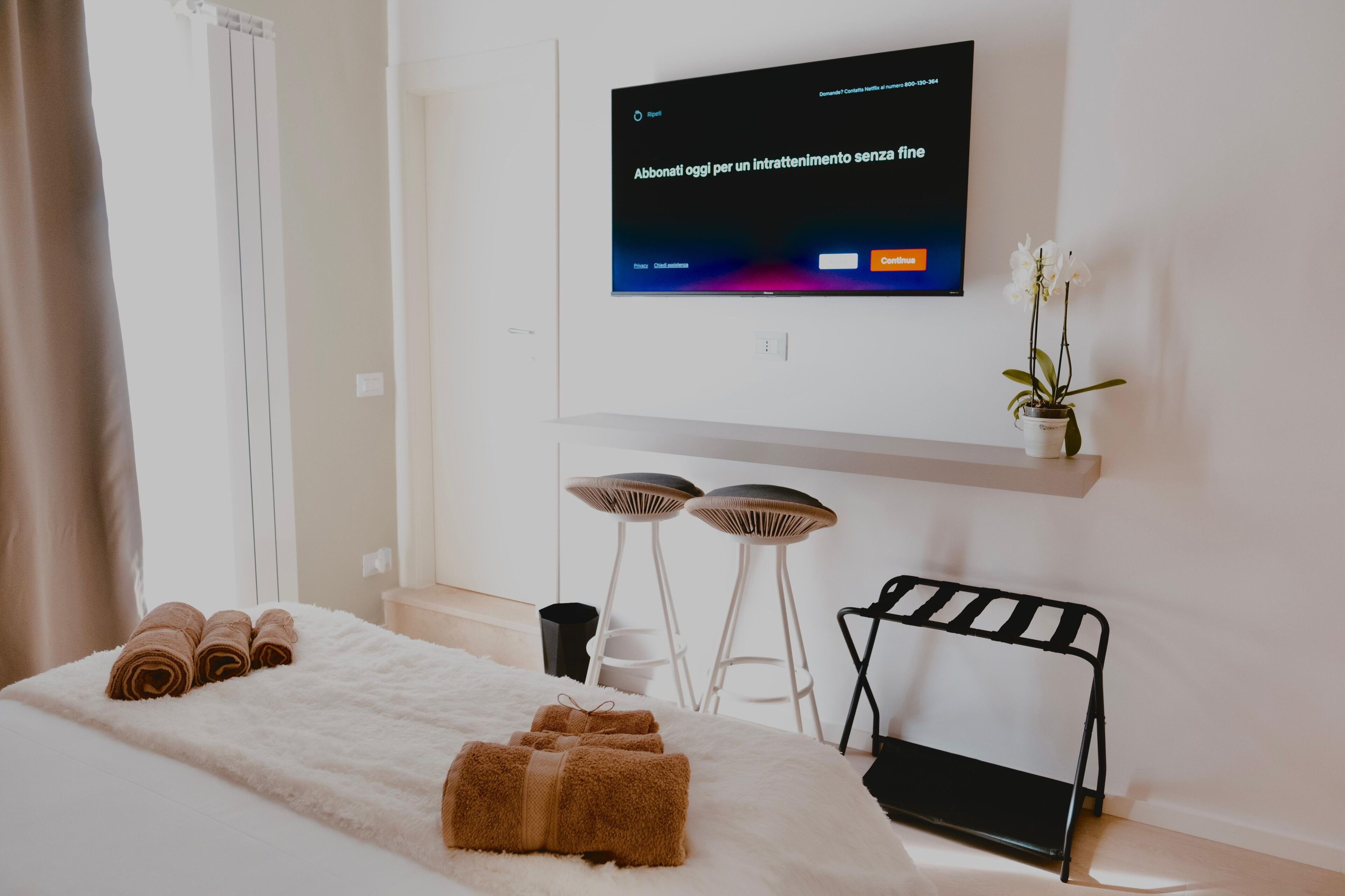 Ett hotellrum med en säng, handdukar, en tv, en liten växt och ett sidobord.