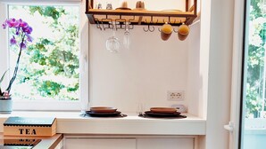 A kitchen with a window, two stools, a tea box, and a shelf with cups and a bowl. - 18zero2 Luxury Rooms (Bari)