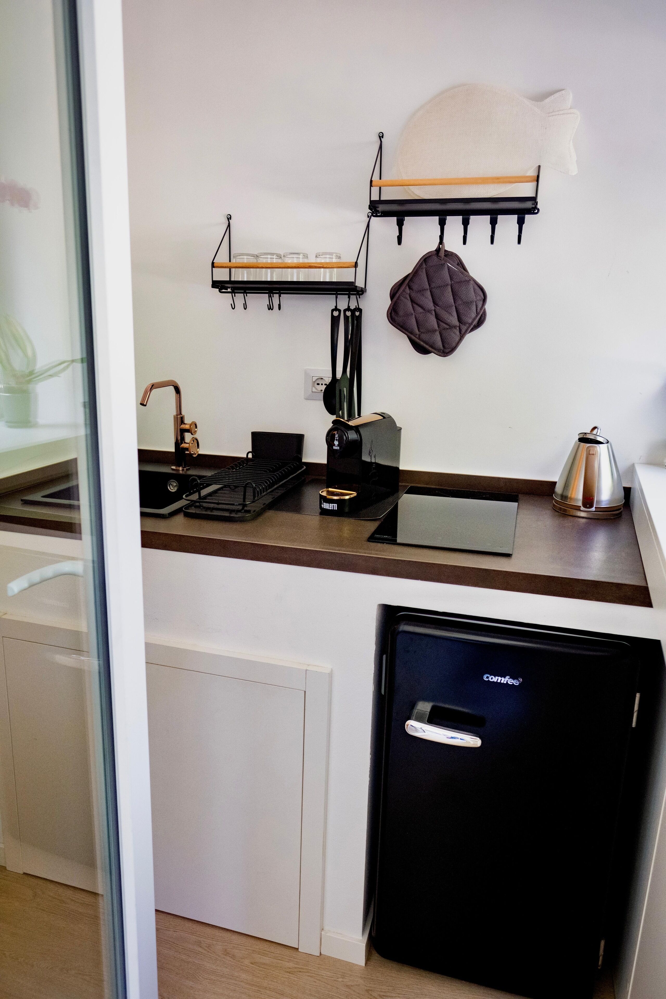 Cocina compacta con cafetera, hervidor y un refrigerador negro.