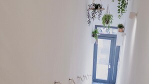 A staircase with white walls, a blue door at the top, and hanging plants. - 18zero2 Luxury Rooms (Bari)