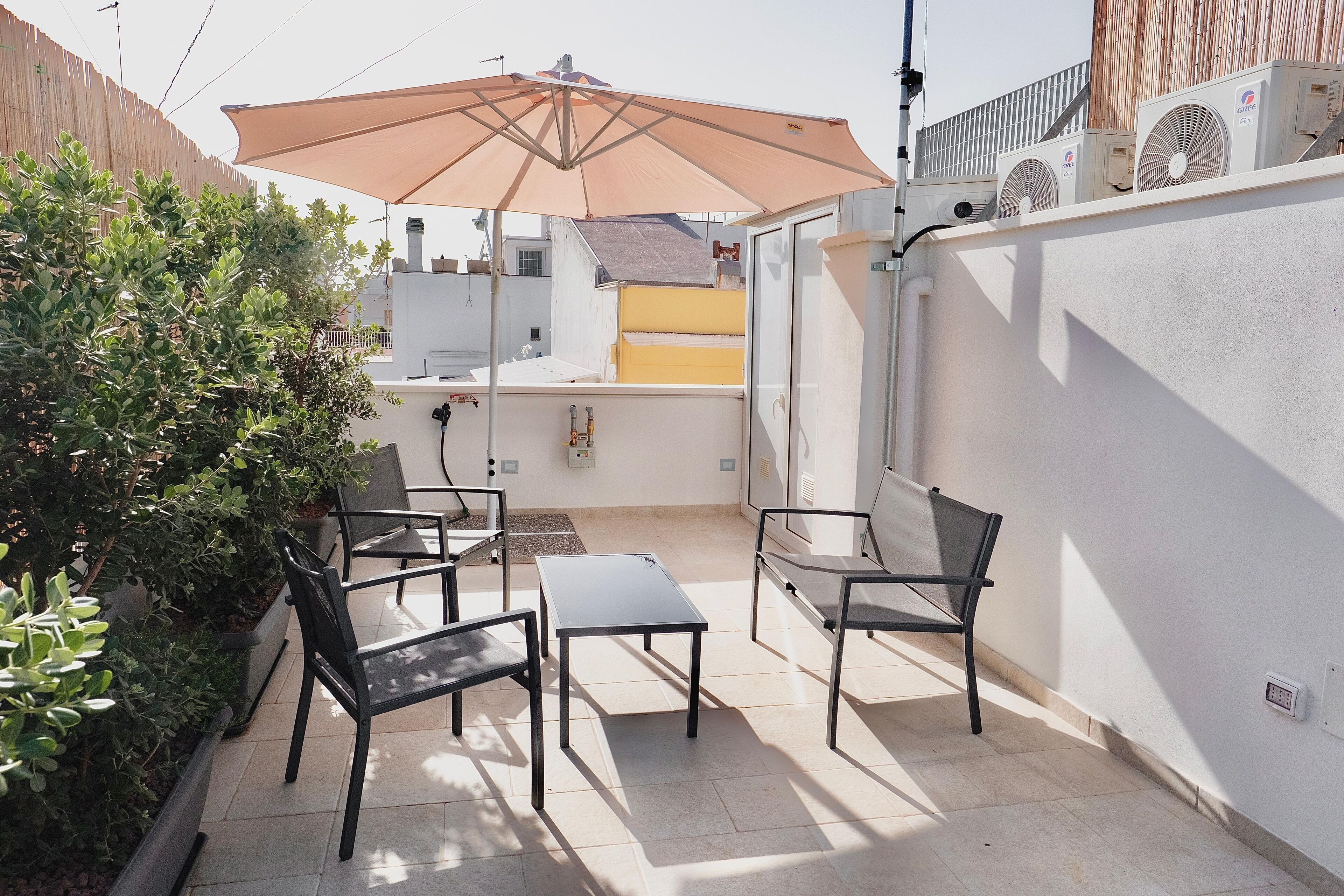 An outdoor patio with a table and chairs, a large umbrella, and a wall-mounted air conditioning unit.