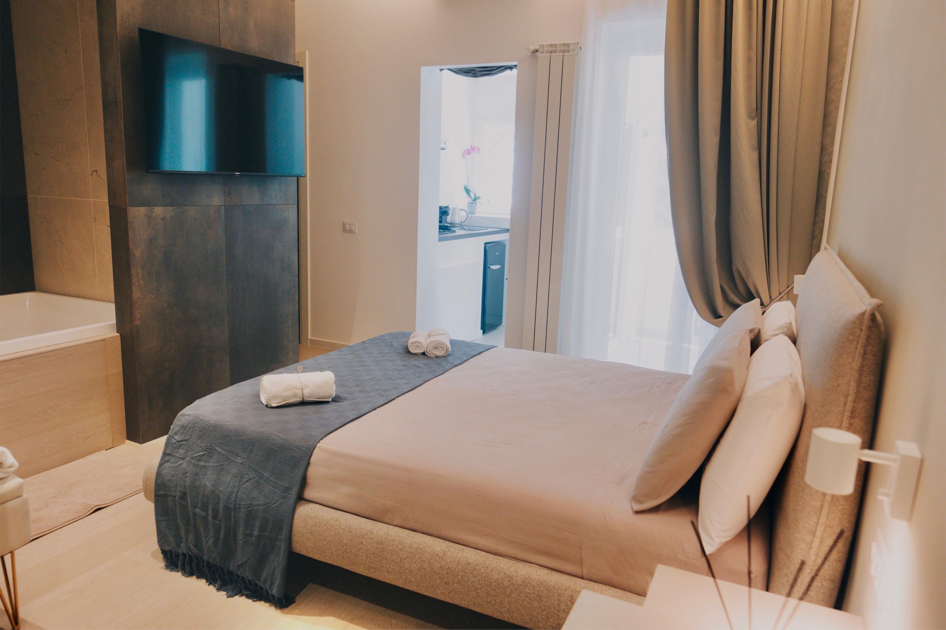A modern hotel room with a large bed, a flat-screen TV mounted on the wall, and a bathroom visible through an open door.
