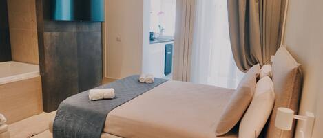 A modern hotel room with a large bed, a flat-screen TV mounted on the wall, and a bathroom visible through an open door.