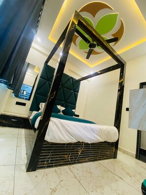 A modern bedroom with a four-poster bed, a green upholstered headboard, and a decorative ceiling light. - Hotel Rising Gest (Ahmedabad)