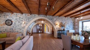 A rustic interior with stone walls, wooden beams, a stone archway, a sofa, a dining table with candles, and a chandelier.