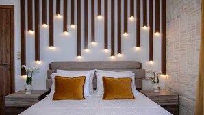 A modern bedroom with a large bed, two nightstands, a wooden slat wall with lights, and a brick wall. - Geroulios Kastro Villa II-Heated* Pool & Jacuzzi (Chania)