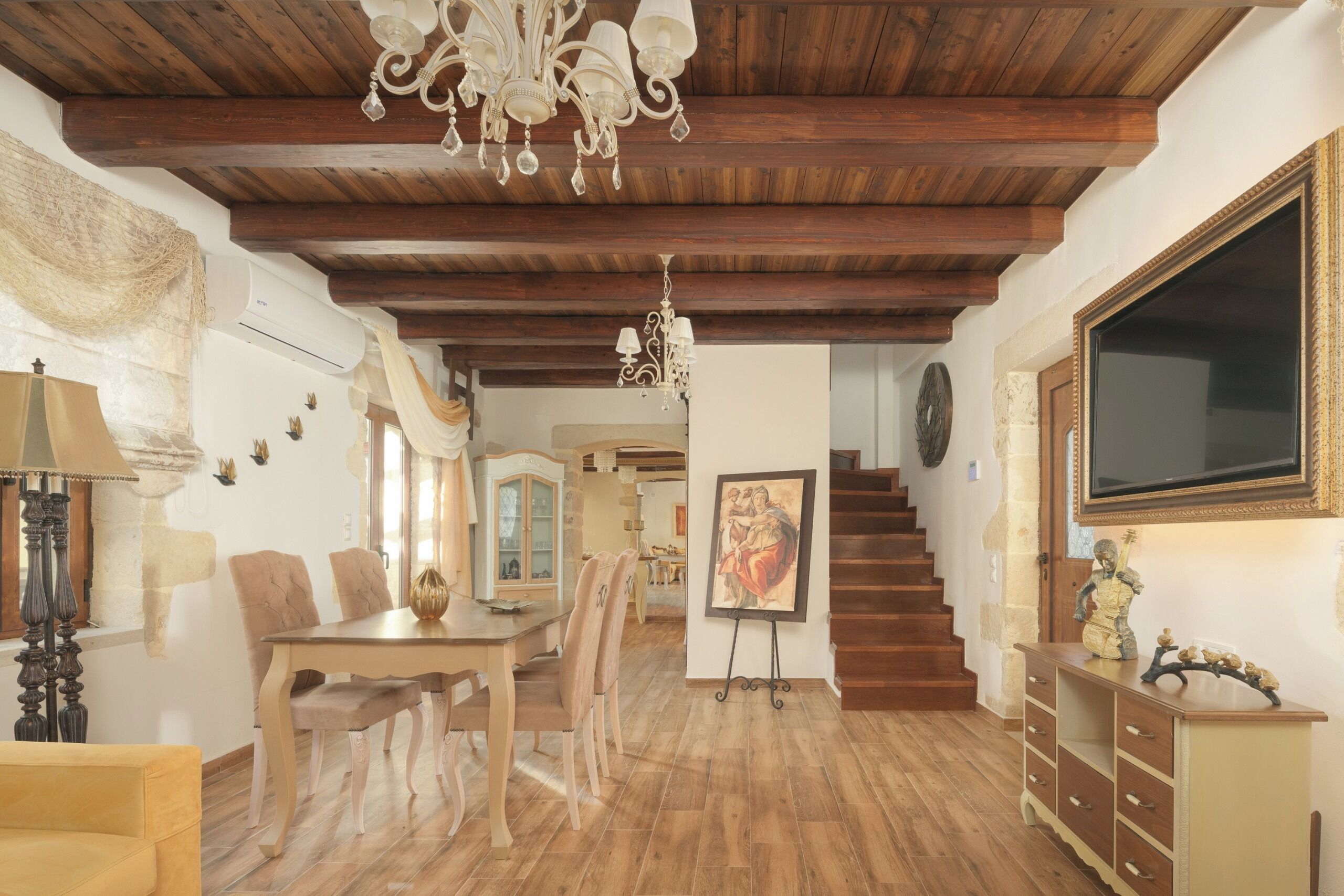 A dining area with a wooden table and chairs, a chandelier, and a staircase leading to another level.