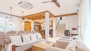 A modern living room with a sofa, coffee table, and chairs, connected to a kitchen and dining area.