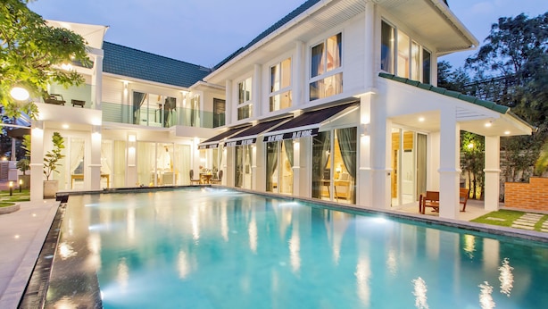 A modern two-story house with a swimming pool, large windows, and outdoor seating areas.