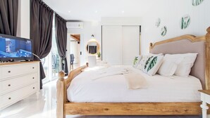 A neatly arranged bedroom with a wooden bed, white bedding, and a television on a dresser.