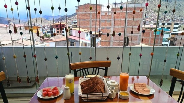 A dining table with breakfast items, a view of buildings, and a balcony with colorful hanging decorations. - Hotel Residencia Inn Cuzco (Cusco)