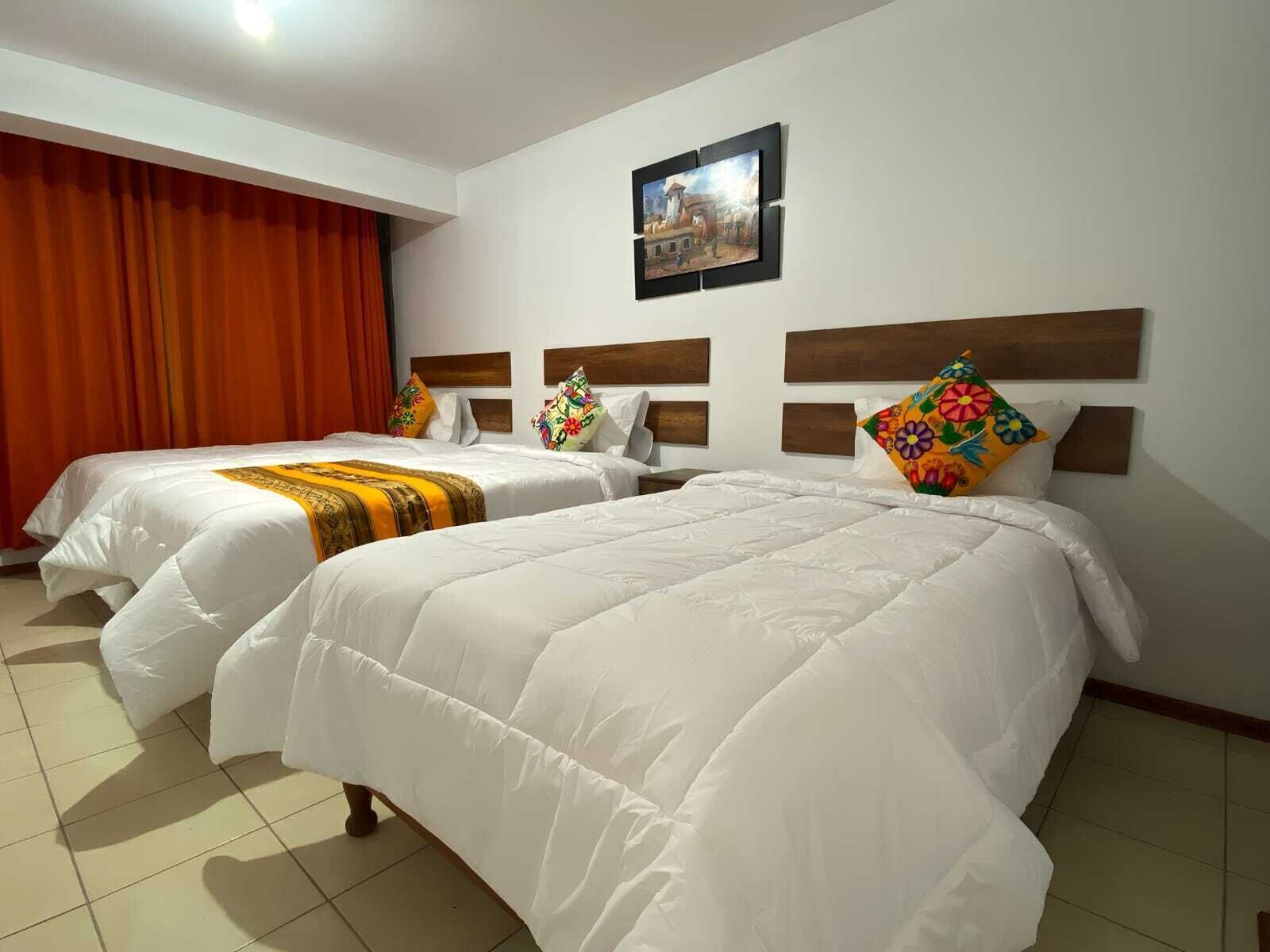 A hotel room with two beds, each with white bedding and colorful pillows. There is a painting on the wall above the beds.