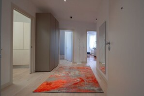 A hallway with a light-colored floor, a red and gray rug, and a large mirror on the right.