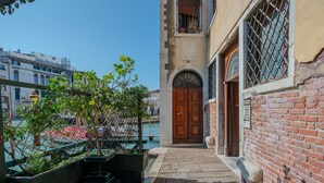 Um beco estreito com uma porta de madeira e um muro de tijolos, que leva a um edifício com varanda.