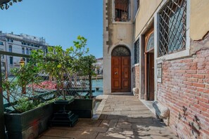 A narrow alleyway with a wooden door and a brick wall, leading to a building with a balcony. - Ca' Marcello Levante (Venezia)